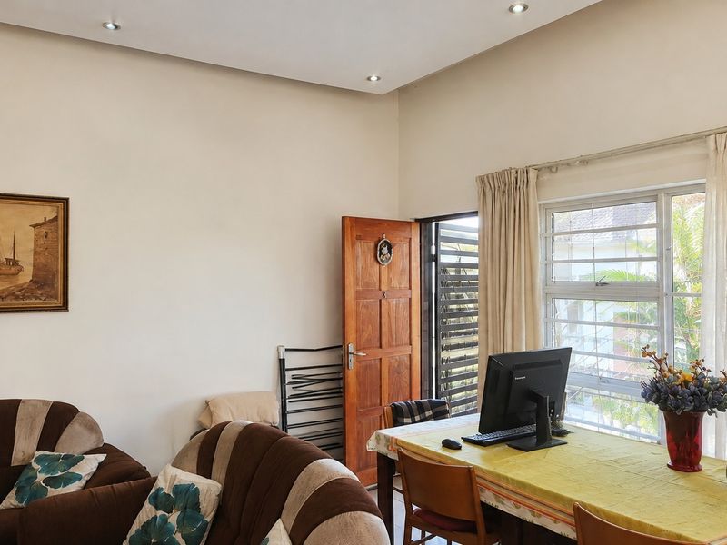 A living area featuring recessed downlights, a timber door with security gate, and a large window with burglar bars providing natural light.
