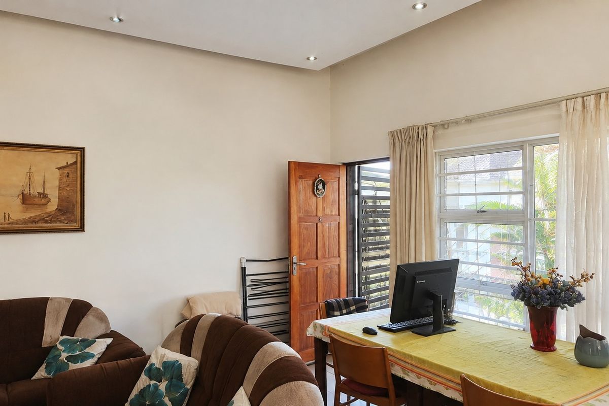 A living area featuring recessed downlights, a timber door with security gate, and a large window with burglar bars providing natural light.