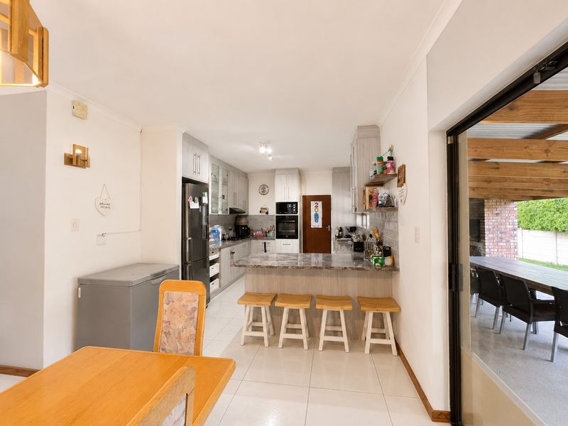 Open-plan kitchen featuring stone countertops, breakfast bar, and built-in appliances, seamlessly connecting to the dining area and outdoor patio through sliding glass doors.