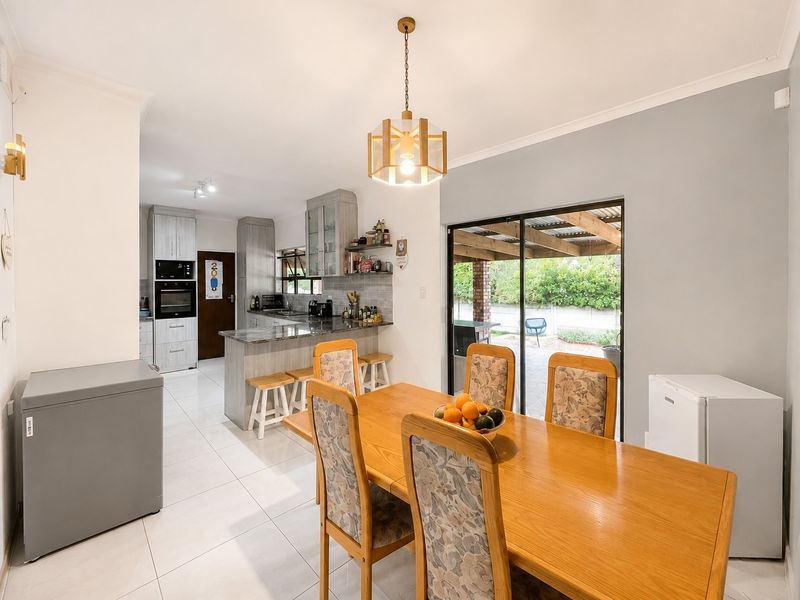 Open-plan kitchen and dining area featuring modern cabinetry, stone countertops, built-in appliances, tiled flooring, and direct access to a covered outdoor patio.