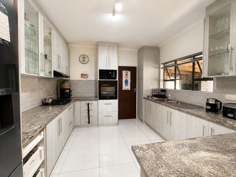 Modern kitchen featuring light wood-grain cabinetry, granite countertops, built-in oven, gas hob, and tiled flooring with ample storage space.