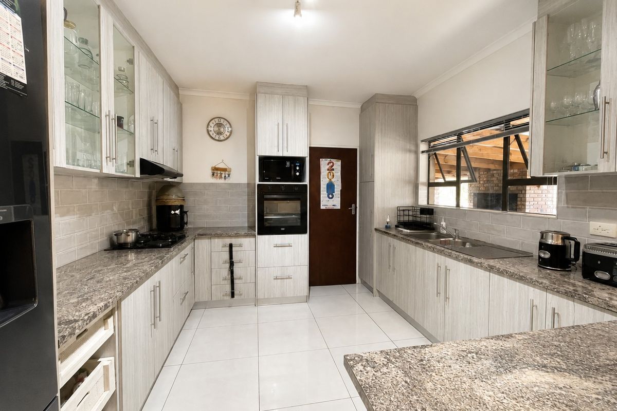 Modern kitchen featuring light wood-grain cabinetry, granite countertops, built-in oven, gas hob, and tiled flooring with ample storage space.