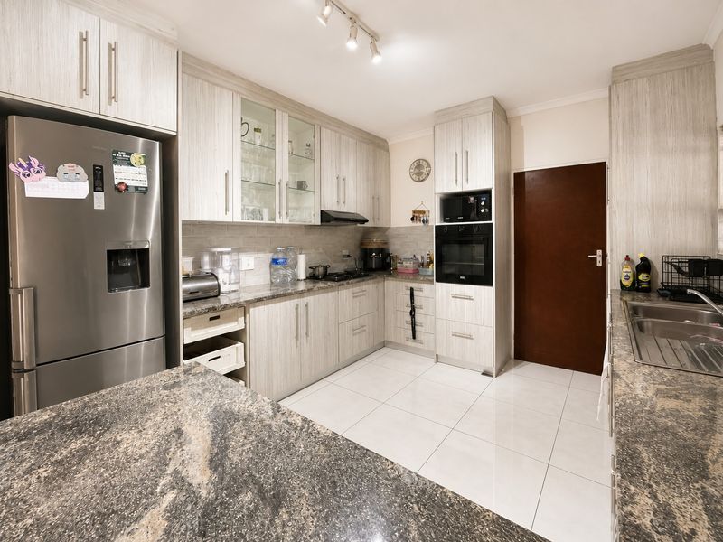 A well-maintained kitchen featuring light wood-grain cabinetry, granite countertops, built-in oven, extractor fan, and tiled flooring with ample storage space.