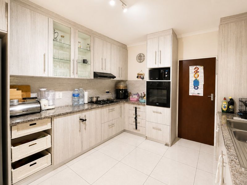Modern kitchen featuring light wood-grain cabinetry, granite countertops, built-in oven and microwave, gas hob, and tiled flooring.