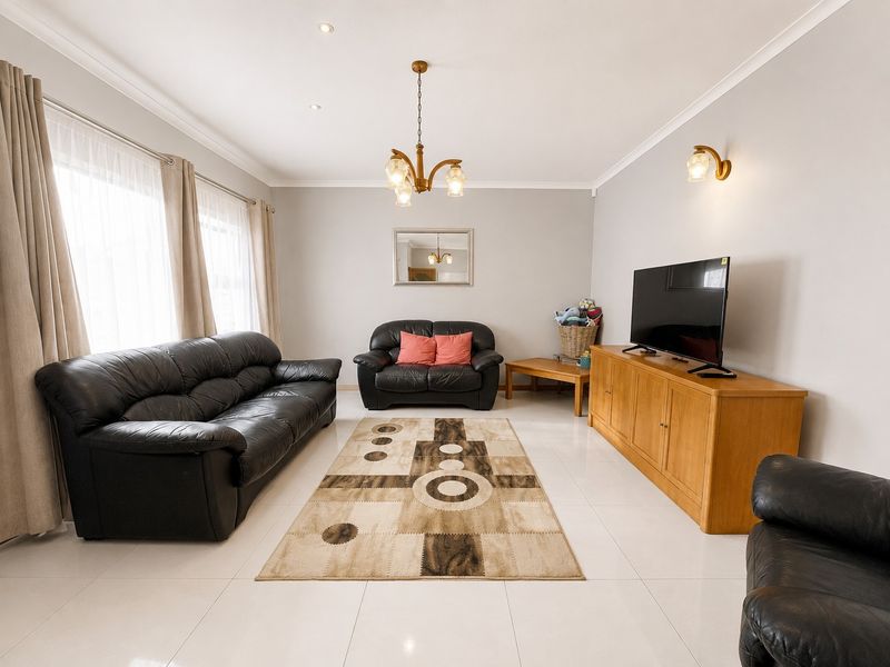 A bright and spacious living room featuring neutral tiled flooring, recessed downlighting, and a classic chandelier, offering a clean and well-maintained living space.
