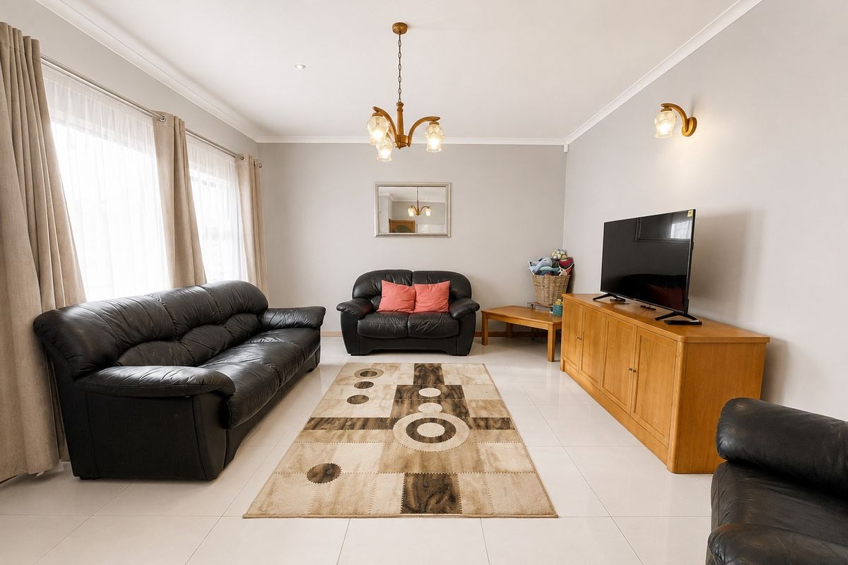 A bright and spacious living room featuring neutral tiled flooring, recessed downlighting, and a classic chandelier, offering a clean and well-maintained living space.