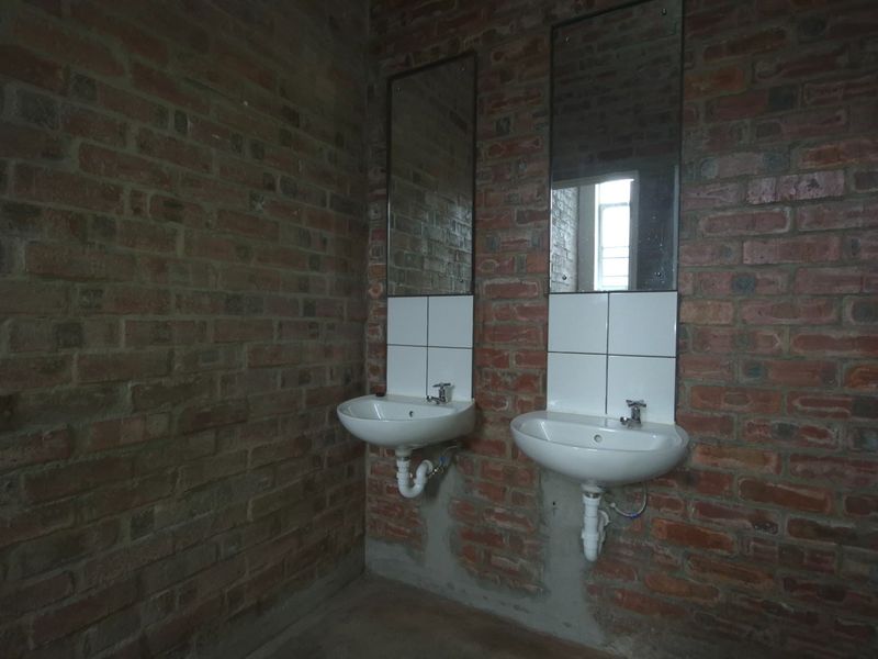 Industrial-style bathroom featuring exposed brick walls, dual wall-mounted ceramic basins with chrome fixtures, and simple mirrors.