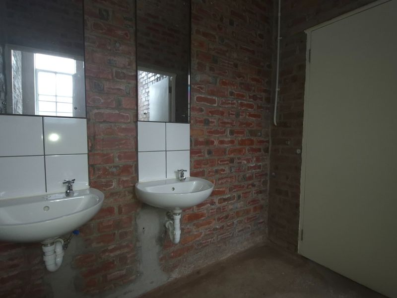 Industrial-style bathroom featuring exposed brick walls, dual wall-mounted basins with chrome fixtures, and a solid door, offering a raw, unfinished aesthetic.