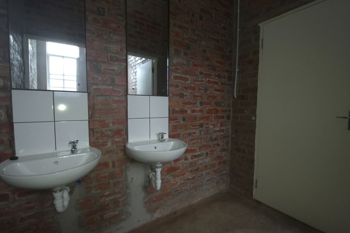 Industrial-style bathroom featuring exposed brick walls, dual wall-mounted basins with chrome fixtures, and a solid door, offering a raw, unfinished aesthetic.