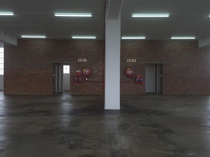 Spacious industrial utility area featuring exposed brick walls, concrete flooring, and integrated fire safety equipment, suitable for warehouse or workshop use.