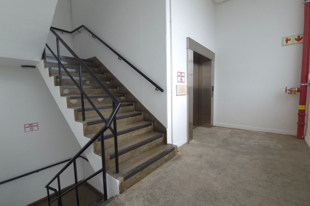 Industrial hallway featuring a concrete staircase with metal handrails, a functional elevator, and exposed fire safety infrastructure.