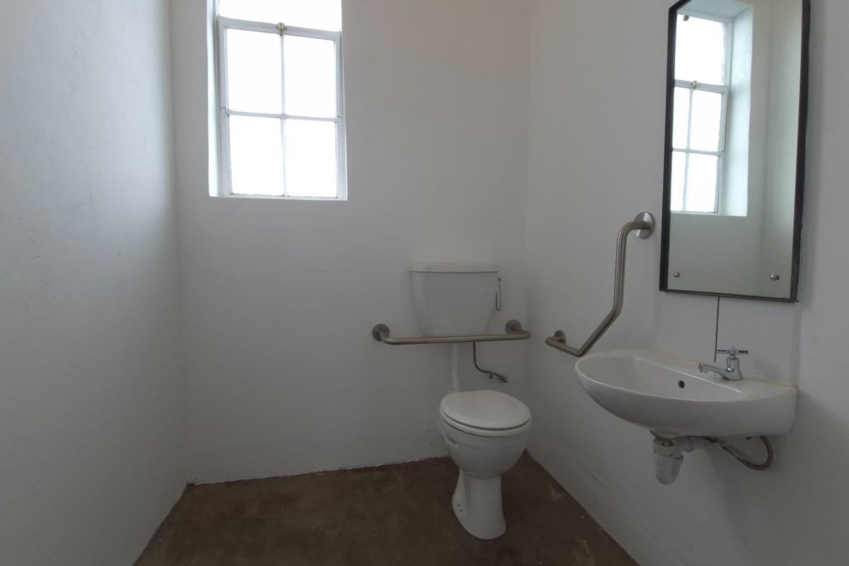 A functional bathroom featuring a toilet, wall-mounted washbasin, and accessibility grab rails, currently requiring floor finishing.