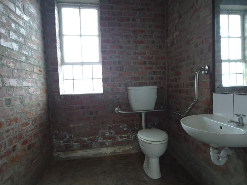 Functional industrial-style bathroom featuring exposed brick walls, a wall-mounted basin, toilet, and accessibility grab rails.