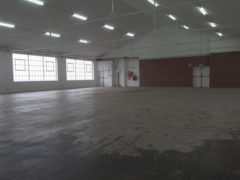 Spacious industrial utility area featuring high ceilings, large steel-framed windows, exposed brick accents, and durable concrete flooring, suitable for various commercial or storage uses.