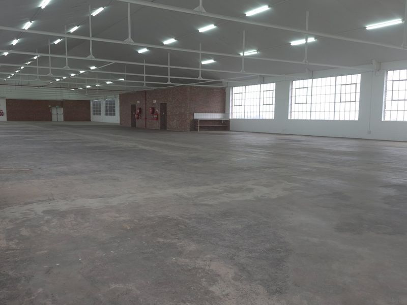 Expansive industrial warehouse space featuring high ceilings with exposed steel trusses, large windows for natural light, and durable concrete flooring.