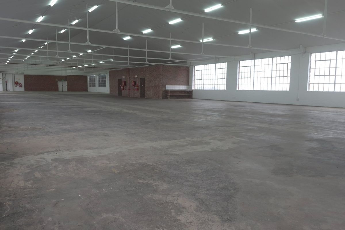 Expansive industrial warehouse space featuring high ceilings with exposed steel trusses, large windows for natural light, and durable concrete flooring.