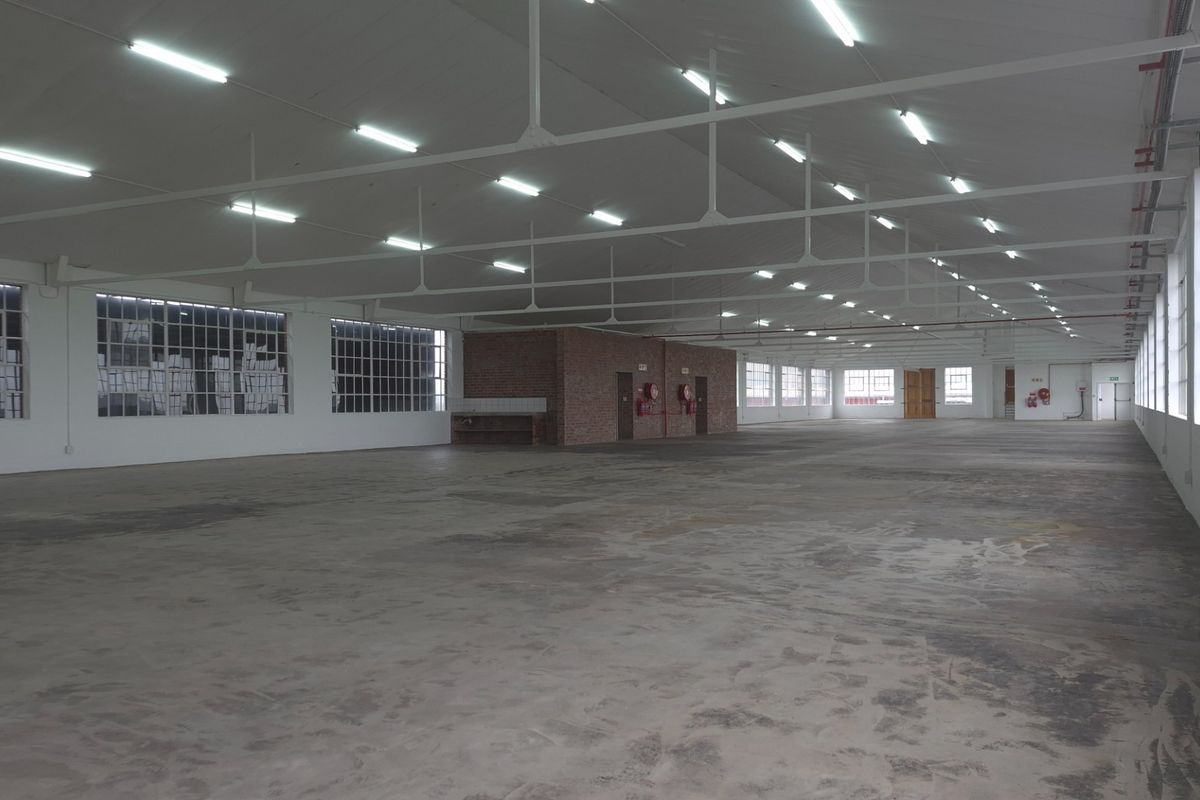 Expansive industrial warehouse space featuring high ceilings with exposed steel trusses, large windows for natural light, and durable concrete flooring.