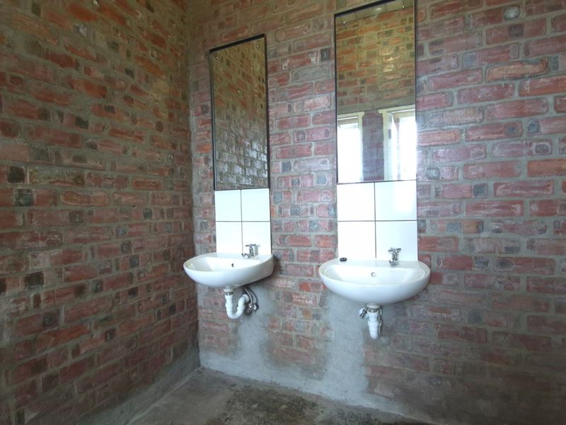 Industrial-style bathroom featuring exposed brick walls, dual wall-mounted ceramic basins with chrome taps, and simple mirrors, currently in an unfinished state.