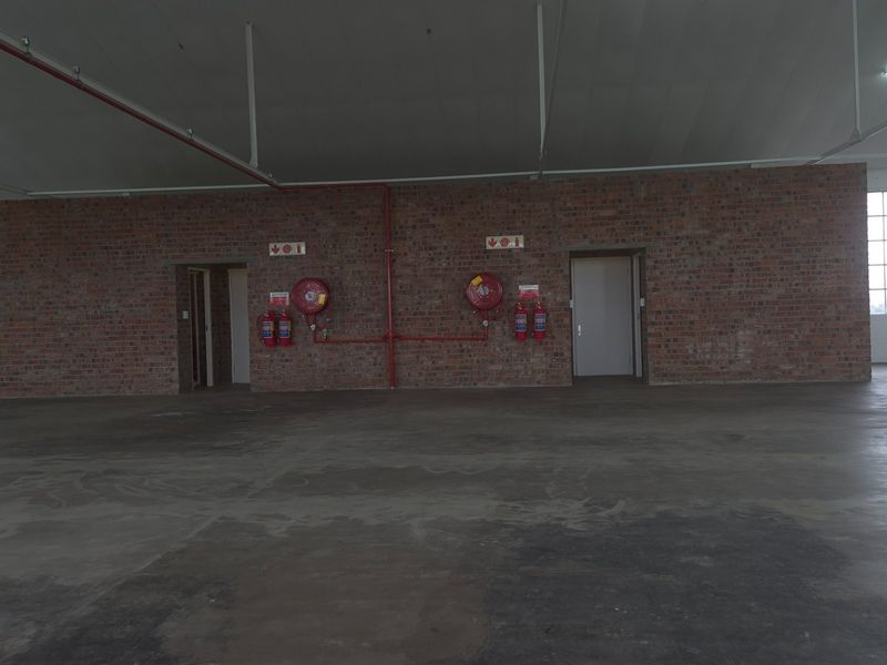 Spacious industrial utility area featuring exposed brick walls, concrete flooring, and integrated fire safety equipment, suitable for warehouse or workshop use.