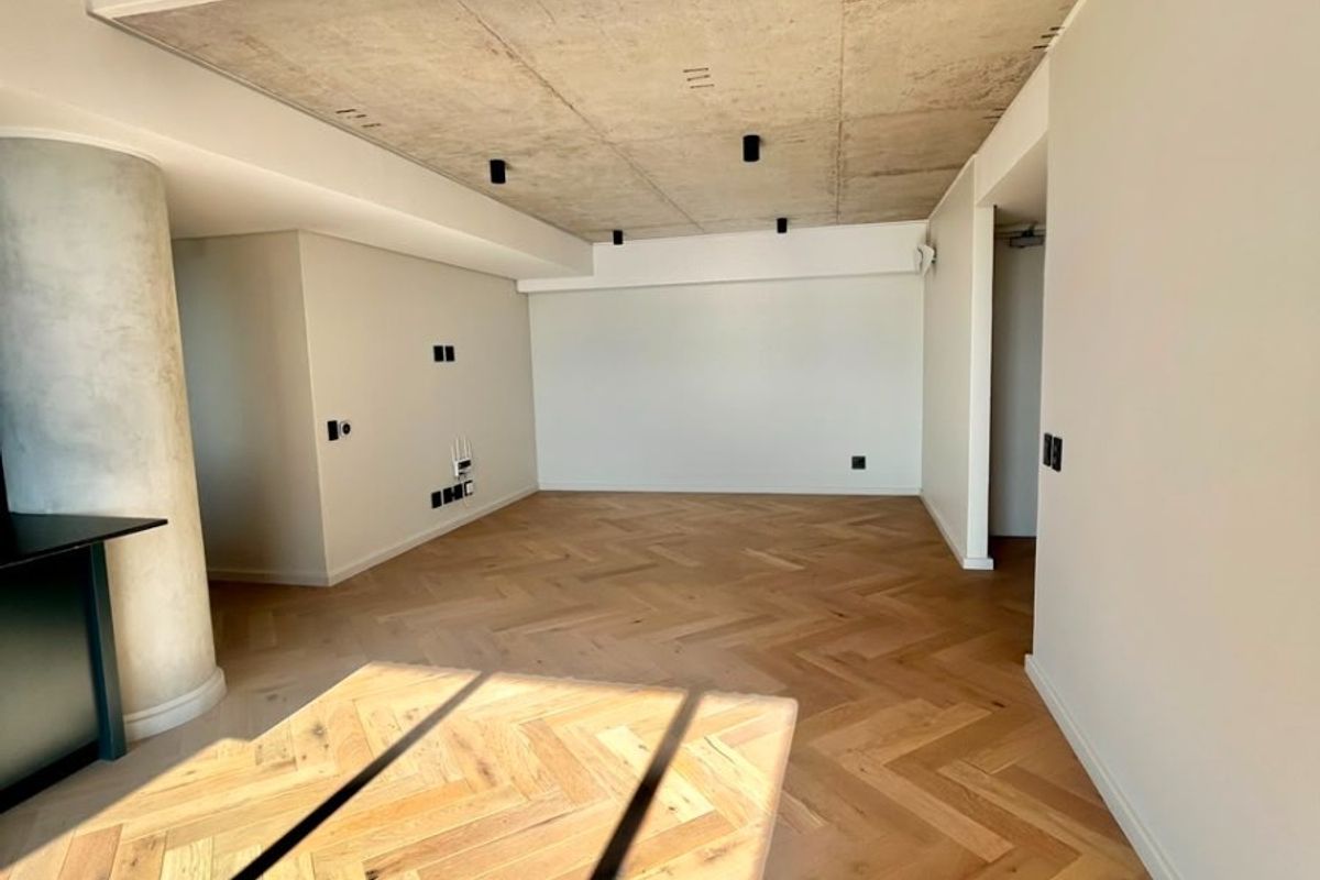 Spacious open-plan living area featuring high-quality herringbone timber flooring, a modern exposed concrete ceiling, and a sleek concrete structural column.