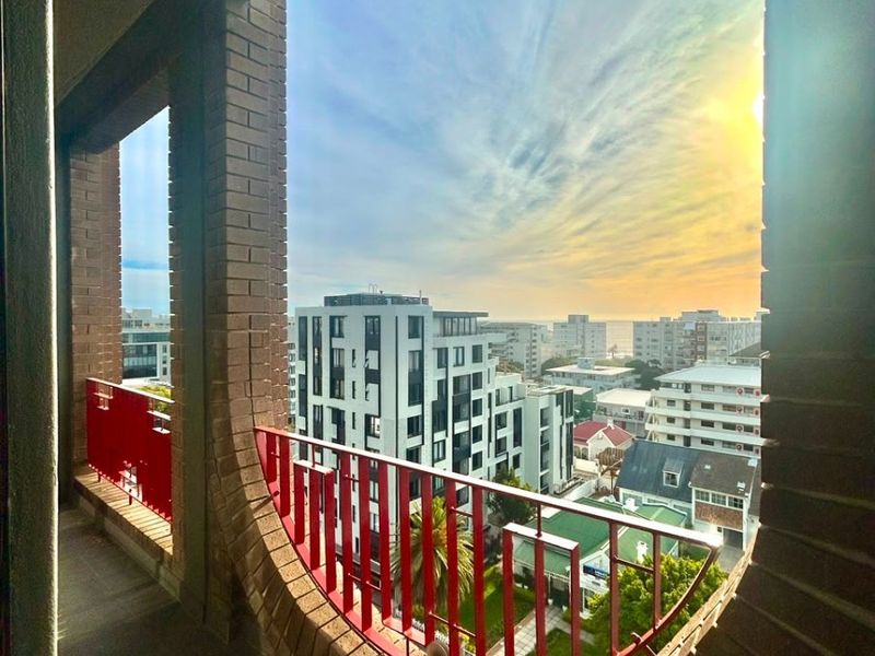 A balcony featuring unique curved brick masonry and a red metal balustrade, offering an elevated urban view.