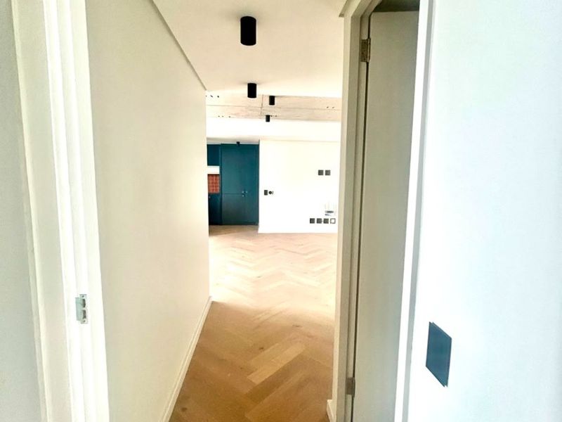 A bright, modern hallway featuring high-quality herringbone timber flooring and minimalist recessed ceiling lighting, leading into an open-plan living area.