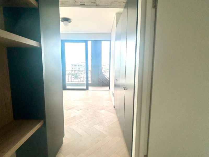 A modern hallway featuring herringbone timber flooring, exposed concrete ceilings, and sleek built-in cabinetry leading towards a bright living area.