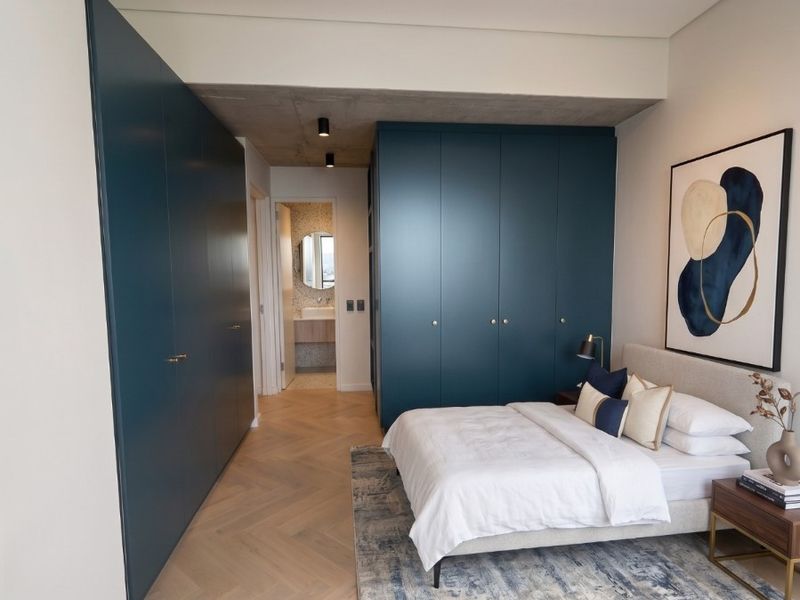 Modern bedroom featuring high-end built-in cabinetry, herringbone timber flooring, and an exposed concrete ceiling, with direct access to an en-suite bathroom.