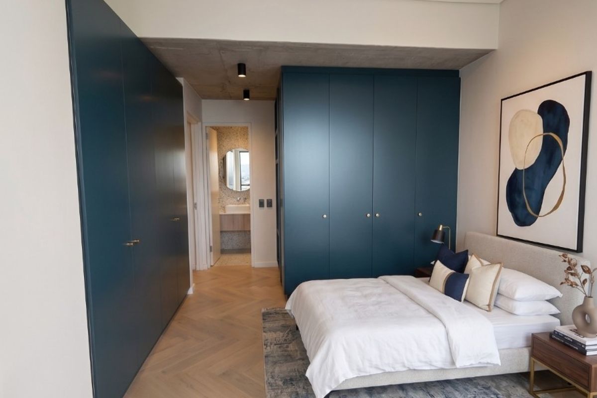 Modern bedroom featuring high-end built-in cabinetry, herringbone timber flooring, and an exposed concrete ceiling, with direct access to an en-suite bathroom.