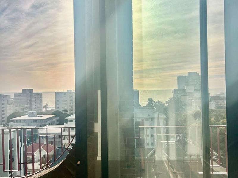 A view from an interior space looking out through sliding glass doors onto a balcony with an urban and coastal cityscape.