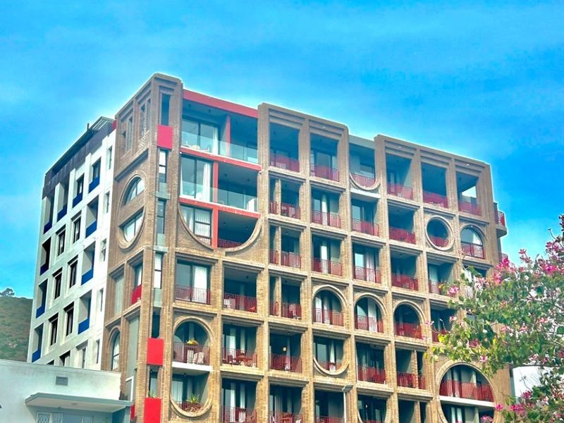 A modern multi-story apartment building featuring a distinctive brick facade with arched balconies, circular architectural details, and integrated planters.