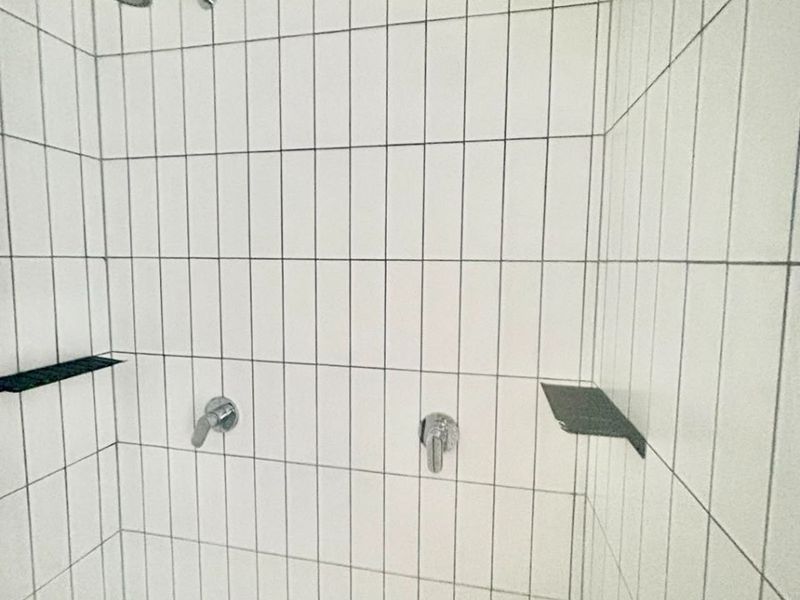 A modern walk-in shower featuring white vertical subway tiles, dual shower heads, and integrated shelving for a clean, minimalist aesthetic.