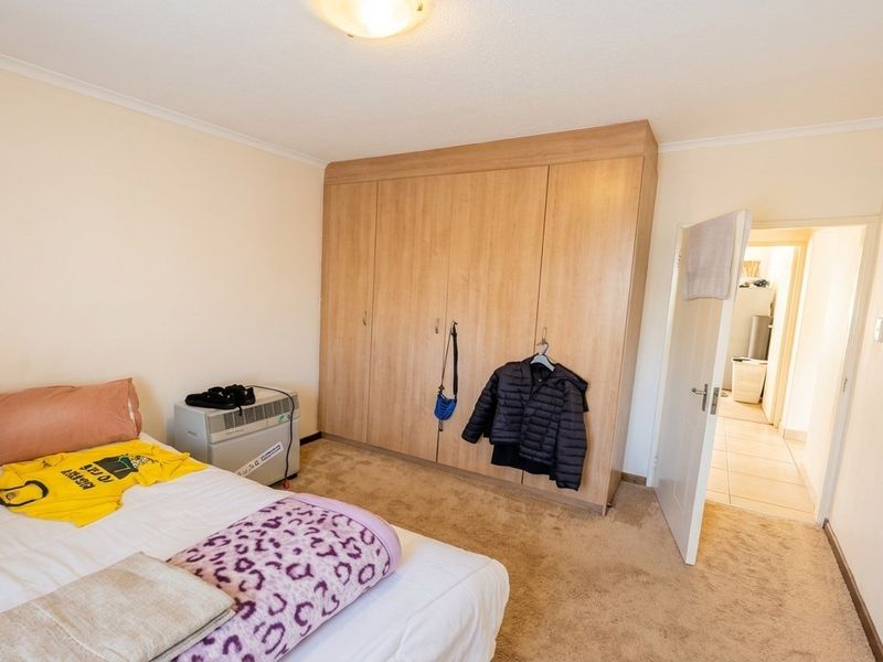 A bedroom featuring a large built-in wooden wardrobe, neutral wall finishes, and carpeted flooring, with an adjacent hallway visible.