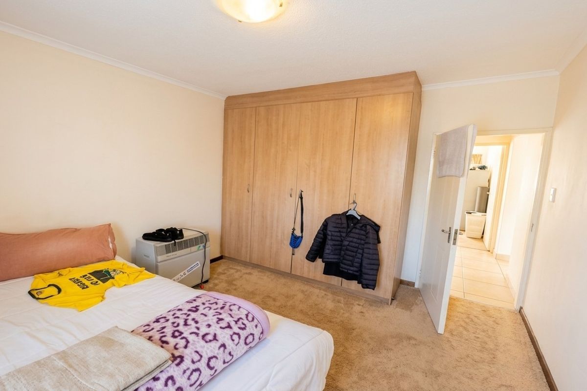 A bedroom featuring a large built-in wooden wardrobe, neutral wall finishes, and carpeted flooring, with an adjacent hallway visible.