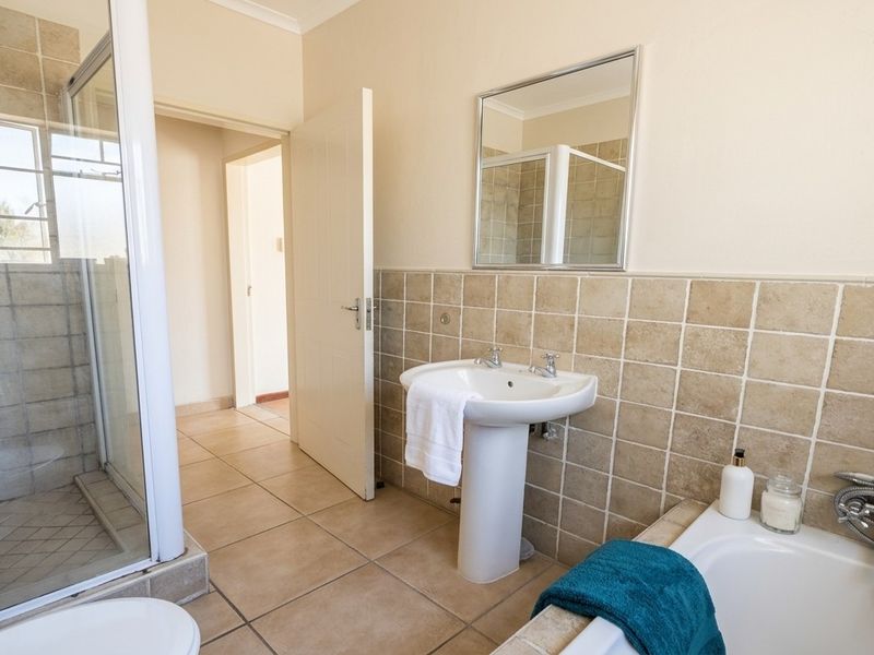 A functional bathroom featuring a pedestal basin, a separate shower enclosure, and a bathtub with neutral wall tiling and floor tiles.
