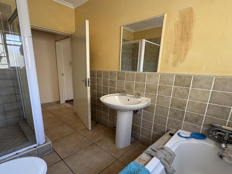 A dated bathroom featuring a pedestal basin, shower enclosure, and built-in bathtub with tiled finishes, requiring cosmetic updates to the walls and fixtures.