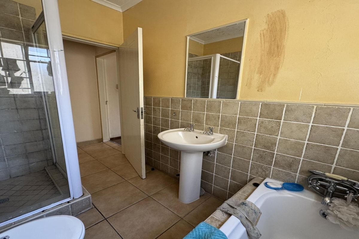 A dated bathroom featuring a pedestal basin, shower enclosure, and built-in bathtub with tiled finishes, requiring cosmetic updates to the walls and fixtures.