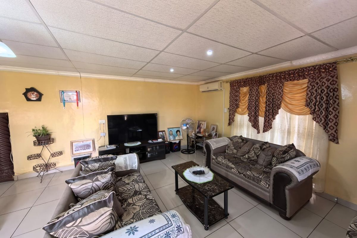 A spacious living room featuring tiled flooring, a suspended ceiling, and a wall-mounted air conditioning unit.