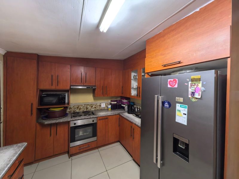 A functional kitchen featuring wooden cabinetry, built-in oven and hob, tiled flooring, and ample storage space, offering potential for modern updates.