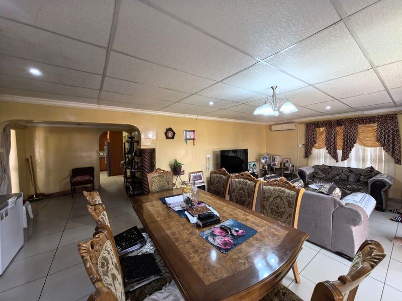 Spacious open-plan living and dining area featuring tiled flooring, a drop ceiling with recessed lighting, and an integrated split-system air conditioner.