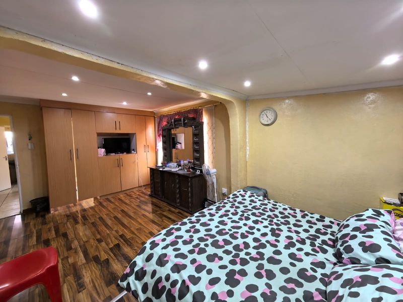 A bedroom featuring built-in wooden cupboards, recessed ceiling lighting, and laminate flooring, offering a functional space with potential for cosmetic updates.