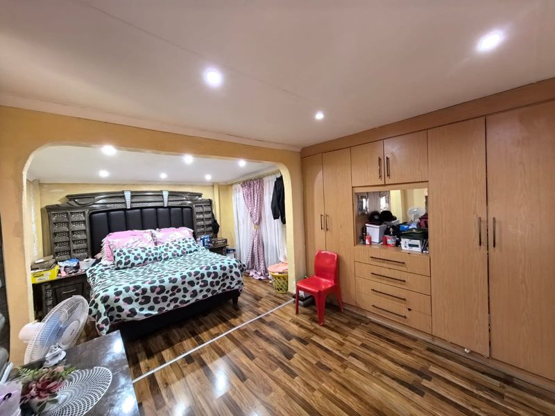 Spacious bedroom featuring extensive built-in wooden cupboards, recessed downlighting, and laminate flooring, with a distinct archway separating the sleeping area.