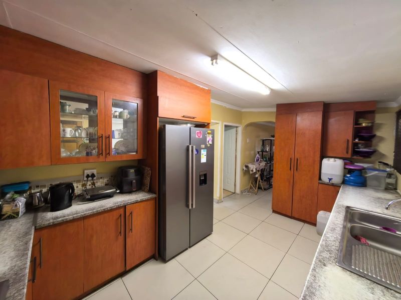 A functional kitchen featuring wood-look laminate cabinetry, granite countertops, a double bowl stainless steel sink, and tiled flooring.