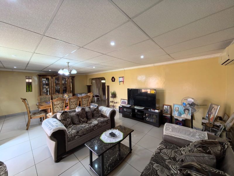 Spacious open-plan living and dining area featuring tiled flooring, a suspended ceiling with recessed lighting, and a wall-mounted air conditioning unit.