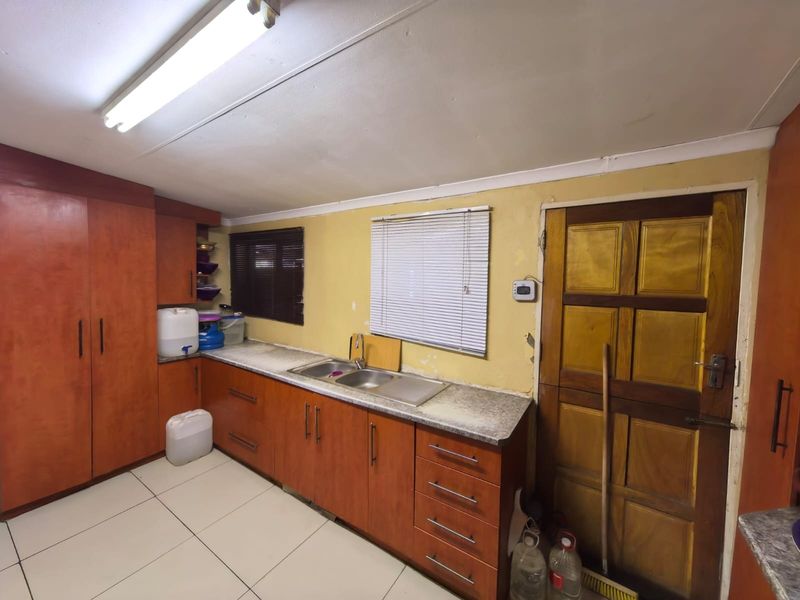 A functional kitchen featuring wood-finish cabinetry, laminate countertops, a double sink, and tiled flooring, currently showing signs of wear and requiring cosmetic updates.