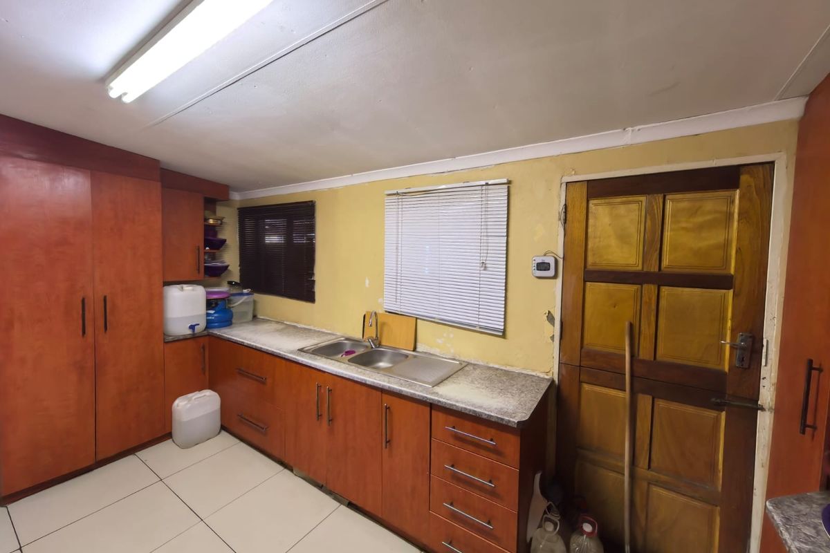 A functional kitchen featuring wood-finish cabinetry, laminate countertops, a double sink, and tiled flooring, currently showing signs of wear and requiring cosmetic updates.