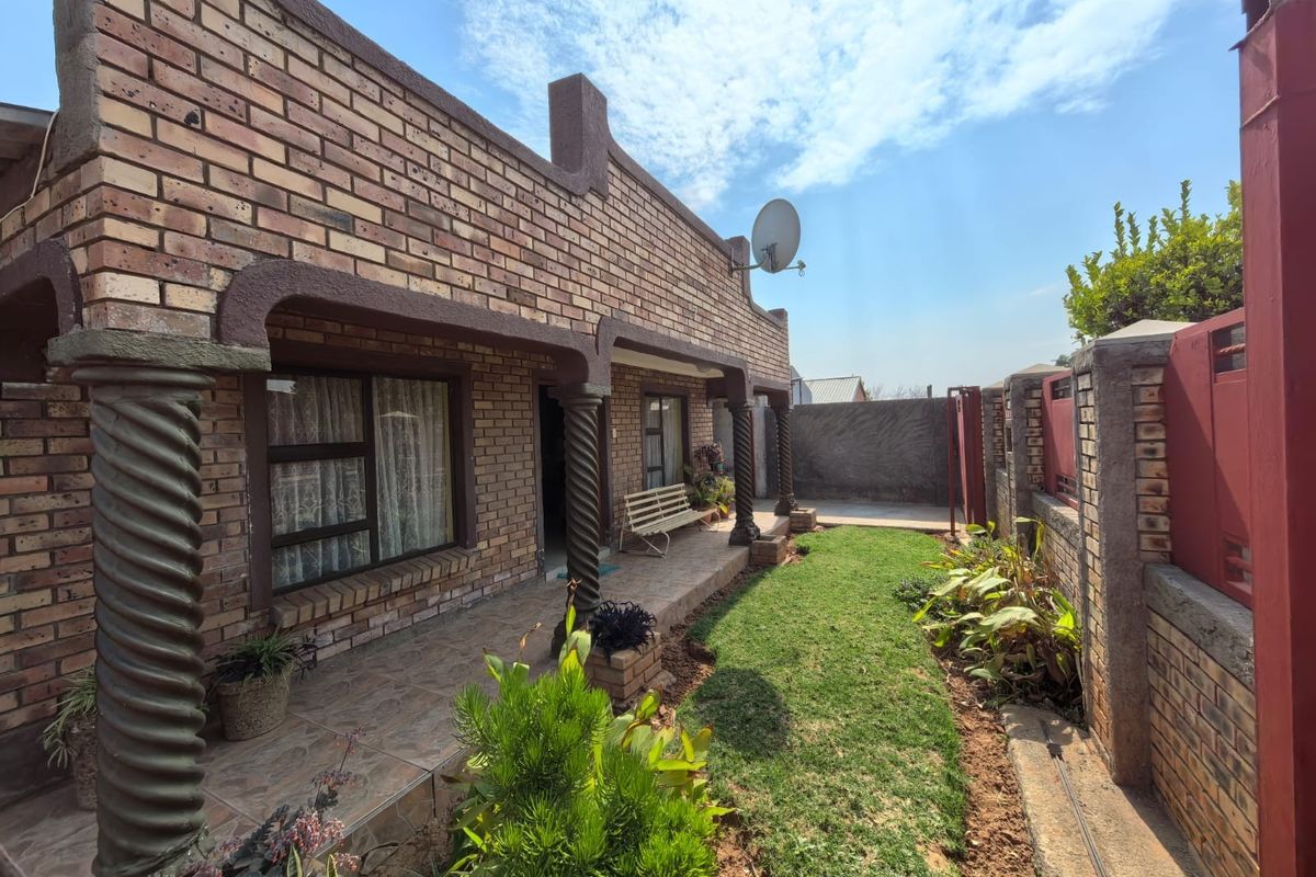 Rear exterior view featuring a face brick facade, covered patio with decorative columns, and a private garden area with boundary walling.