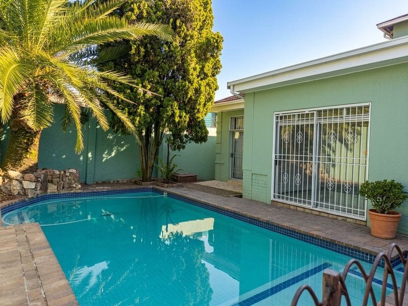 A well-maintained swimming pool area featuring a paved surround, boundary wall, and direct access to the home via a sliding glass door with security gate.