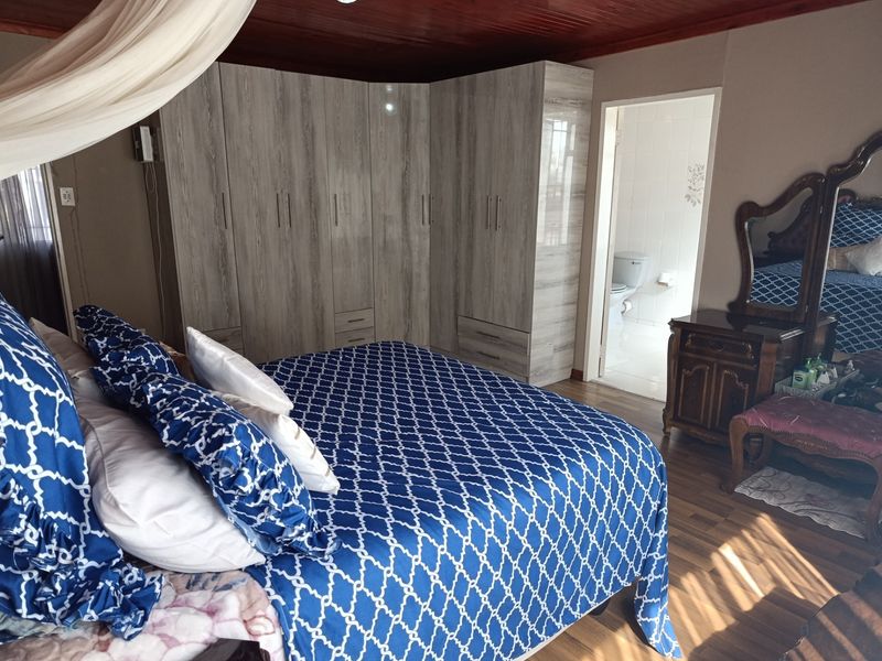 Spacious bedroom featuring built-in cupboards, warm timber ceiling, laminate flooring, and direct access to an en-suite bathroom.
