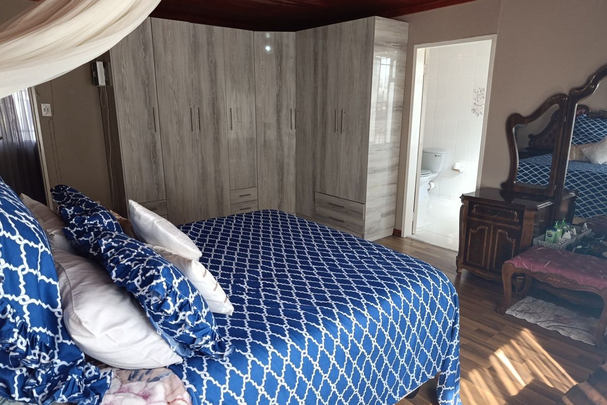 Spacious bedroom featuring built-in cupboards, warm timber ceiling, laminate flooring, and direct access to an en-suite bathroom.